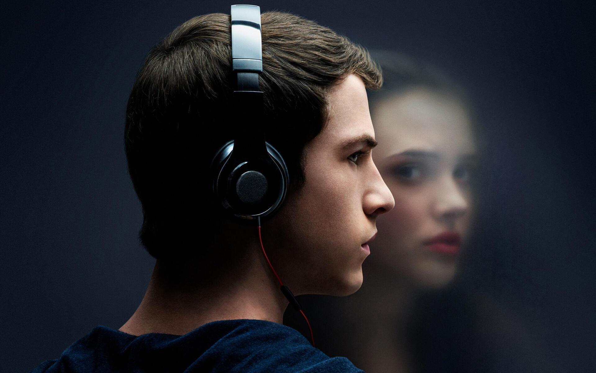 HD PC desktop wallpaper featuring a close-up of a young man wearing headphones with a blurred reflection of a girl in the background, inspired by 13 Reasons Why.