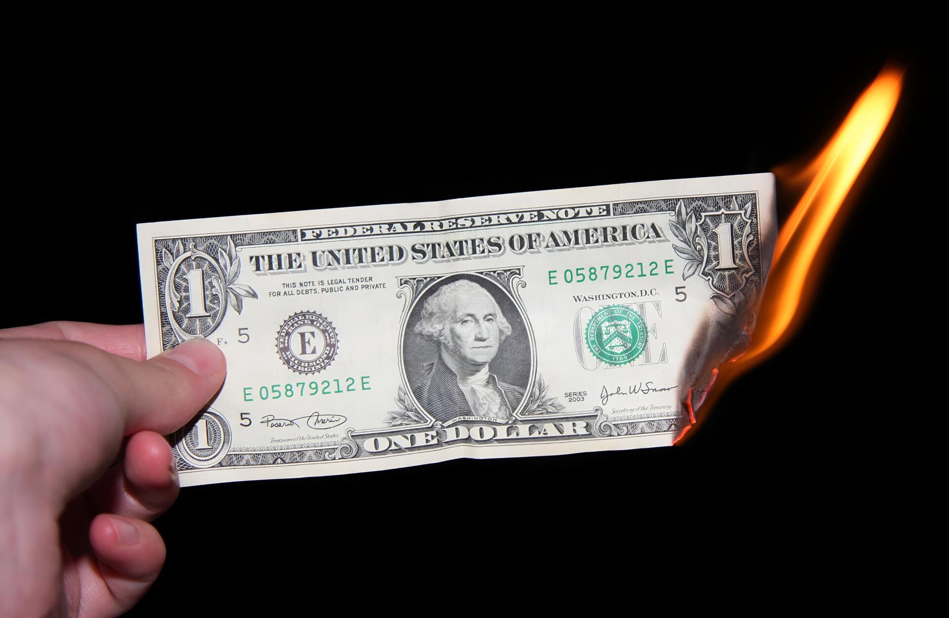 HD PC desktop wallpaper: a hand holds a burning US one-dollar banknote, flames consuming the edge against a black background.