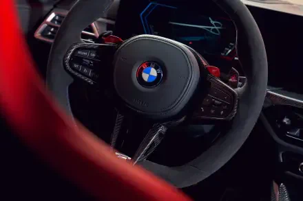 Close-up of a BMW M3 CS Touring steering wheel, showcasing its sleek design and modern features, set against a backdrop of a high-definition PC desktop wallpaper.