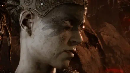 Close-up of Senua from the video game Hellblade: Senua's Sacrifice, showcasing her intense expression and detailed facial markings against a dark, atmospheric background.