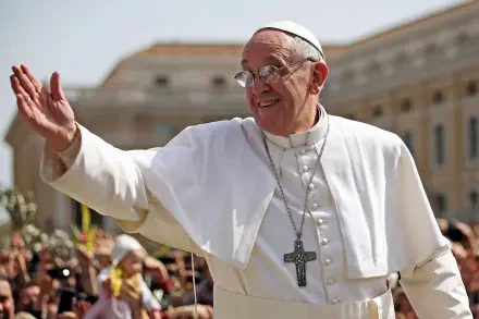 Pope Francis smiles and waves at a crowd, dressed in white vestments with a cross necklace, set against a backdrop of a sunlit Vatican, perfect for a religious-themed desktop wallpaper.