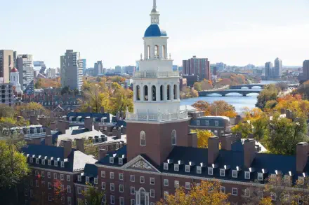 A vibrant HD desktop wallpaper showing the Harvard University campus with the city of Cambridge and Charles River in the background under a clear sky.