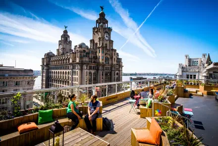 4K Ultra HD cityscape of Liverpool featuring iconic man-made architecture and a rooftop lounge with people enjoying the view under a bright blue sky.
