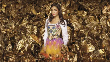 Woman in a colorful feathered costume amid a backdrop of golden leaves — The Hunger Games: The Ballad of Songbirds & Snakes 8K Ultra HD PC desktop wallpaper.