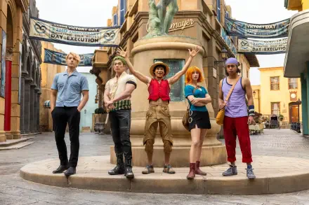 HD PC desktop wallpaper of One Piece (Live Action) TV show characters lined up around a fountain in a bright, colorful town square.