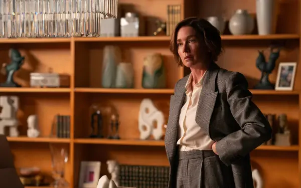 Julianne Nicholson stands thoughtfully in a modern room filled with decorative pieces, featured in the TV show Paradise (2025). The image serves as a striking HD wallpaper.