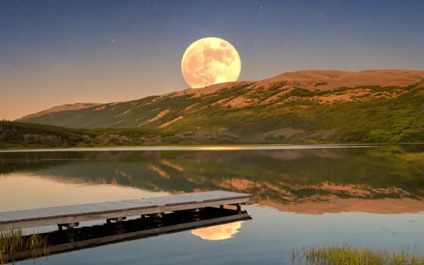 A stunning harvest moon rises over tranquil waters, casting reflections on the lake, with mountains in the background, creating a serene nature scene. 4K Ultra HD wallpaper.