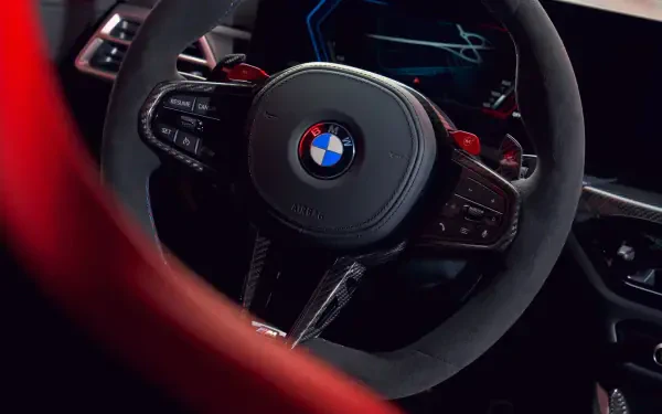 Close-up of a BMW M3 CS Touring steering wheel, showcasing its sleek design and modern features, set against a backdrop of a high-definition PC desktop wallpaper.