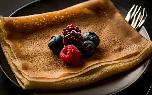 A delicious crêpe topped with fresh berries, presented on a sleek black plate, serves as an enticing 4K Ultra HD wallpaper and background.