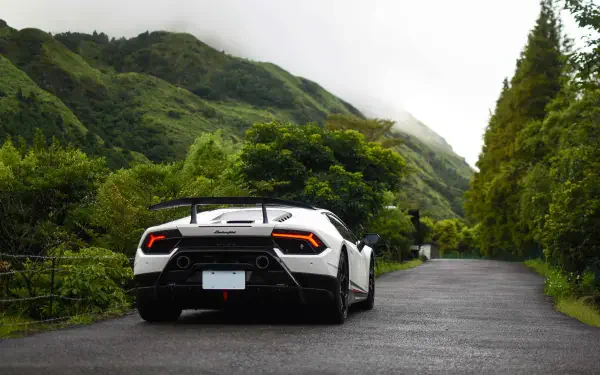 Rear view of a white Lamborghini Huracan sports car on a wet mountain road, surrounded by lush green hills — 5K Ultra HD PC desktop wallpaper/background.