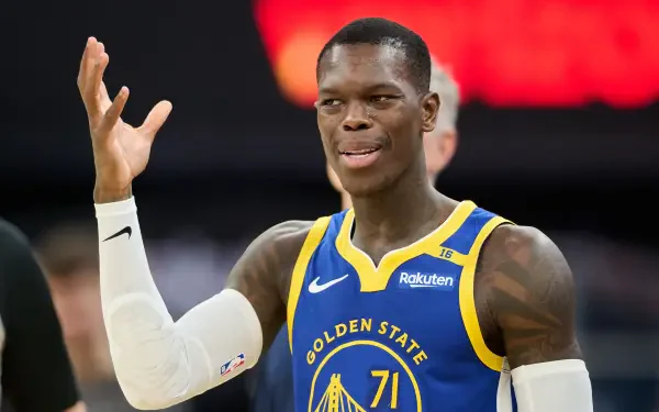 Dennis Schröder gestures playfully while wearing a Golden State Warriors jersey during an NBA game. This HD image captures the dynamic energy of basketball.