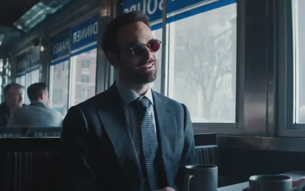 A stylish scene from Daredevil: Born Again, featuring a man in a suit with sunglasses, sitting in a diner, exuding confidence and charm. HD wallpaper for fans of the show.