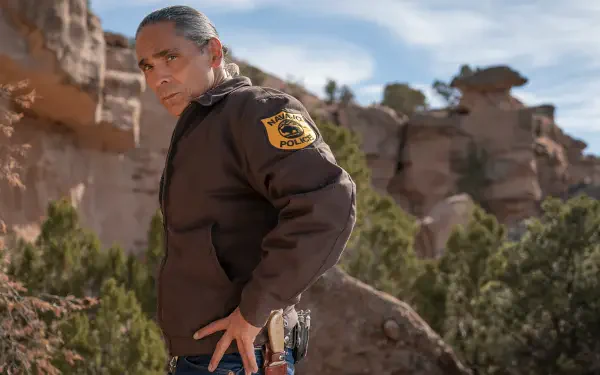 Zahn McClarnon in character as a law enforcement officer in Dark Winds, set against a striking desert landscape, showcasing the show's captivating atmosphere. HD wallpaper.