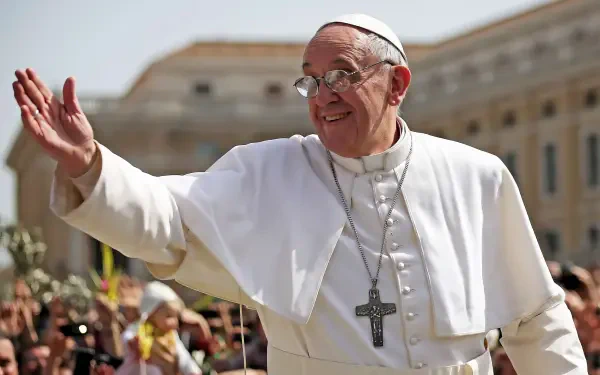 Pope Francis smiles and waves at a crowd, dressed in white vestments with a cross necklace, set against a backdrop of a sunlit Vatican, perfect for a religious-themed desktop wallpaper.