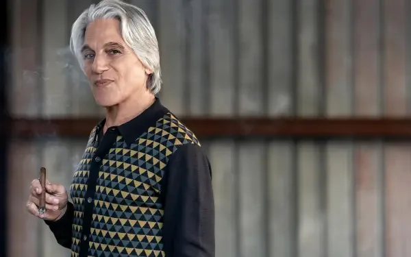 A character from the TV show Power Book III: Raising Kanan poses confidently, wearing a patterned vest, with a subtle smile against a textured backdrop. HD desktop wallpaper.