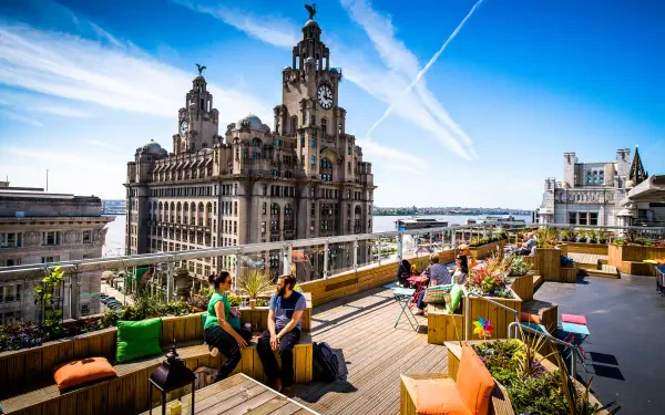 4K Ultra HD cityscape of Liverpool featuring iconic man-made architecture and a rooftop lounge with people enjoying the view under a bright blue sky.