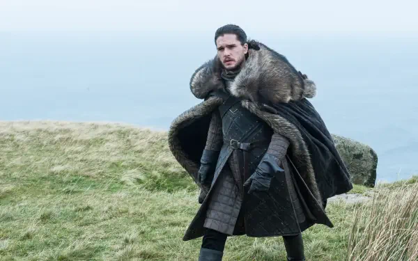 HD PC desktop wallpaper featuring Jon Snow from Game of Thrones standing on a grassy cliff with a vast, misty landscape in the background.