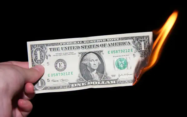 HD PC desktop wallpaper: a hand holds a burning US one-dollar banknote, flames consuming the edge against a black background.