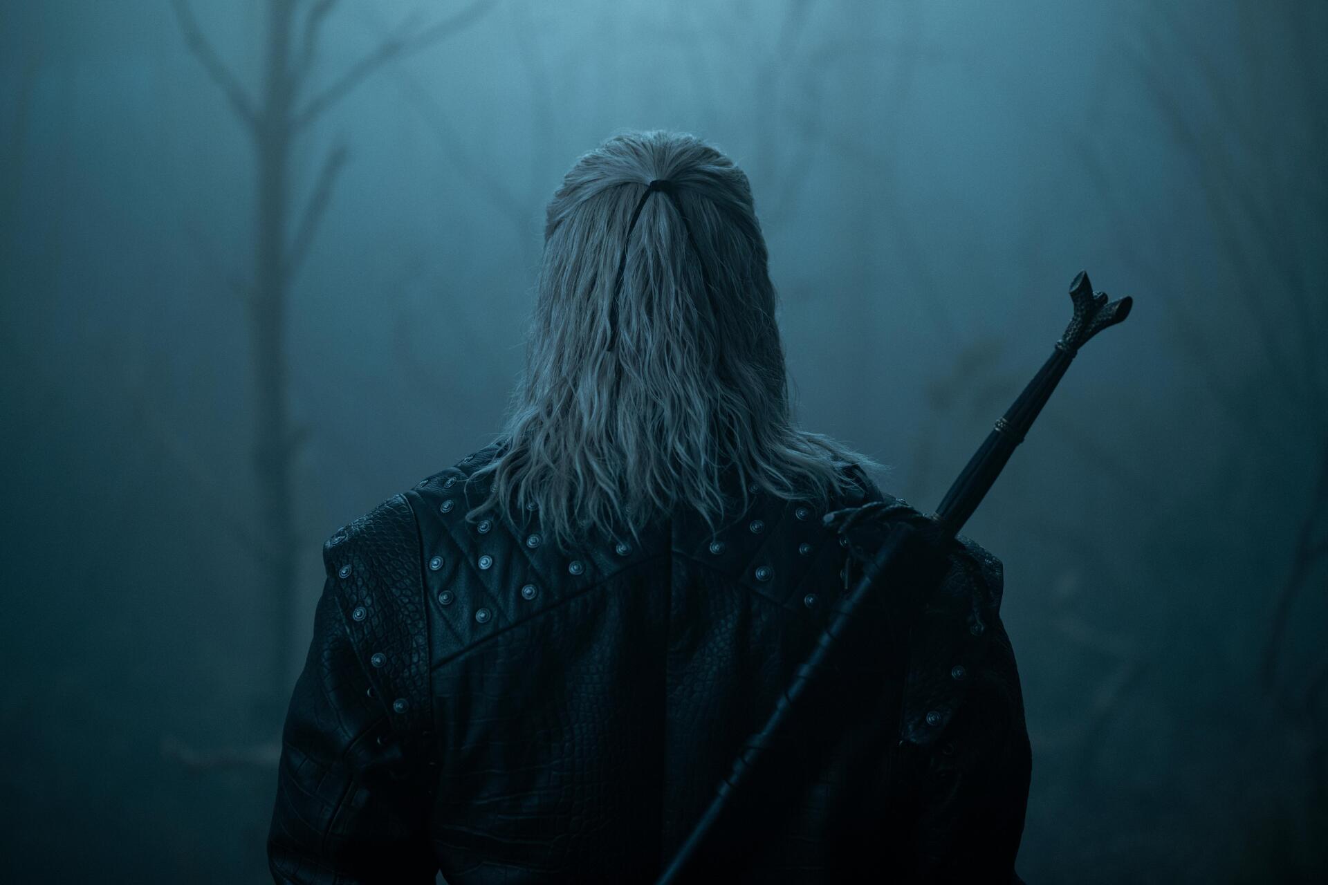 Rear view of Geralt of Rivia from The Witcher TV show, sword on his back in a misty blue forest — 8K Ultra HD PC desktop wallpaper/background.