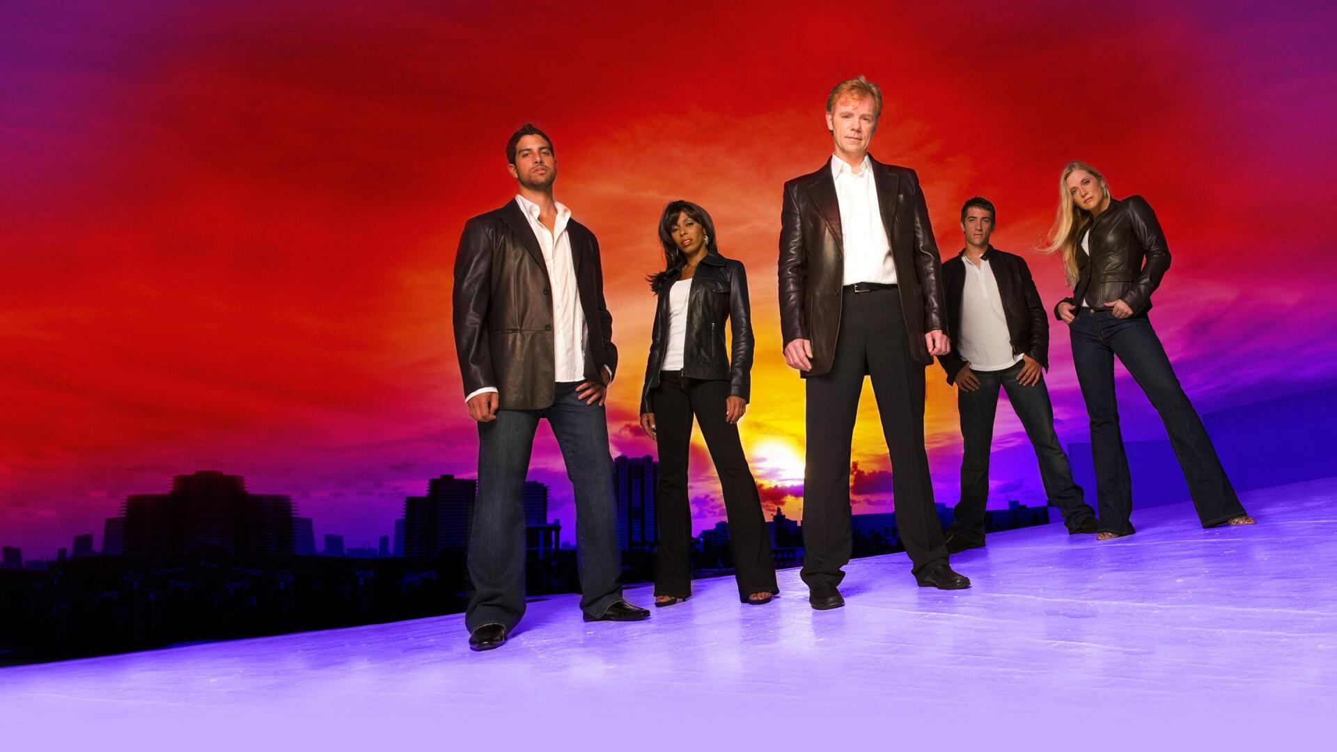 CSI: Miami 2K Quad HD PC desktop wallpaper — five forensic investigators stand on a reflective surface before a vivid red-orange sunset and silhouetted Miami skyline.