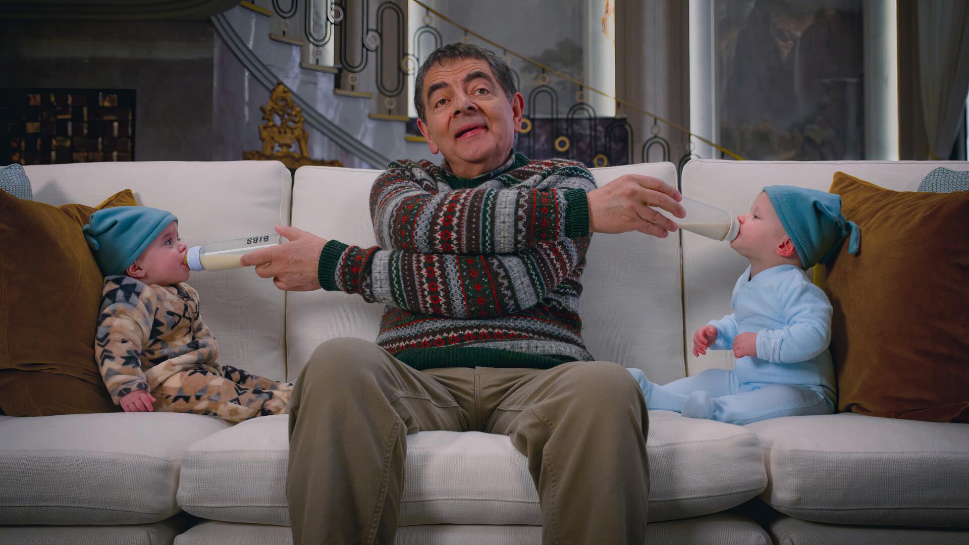 4K Ultra HD PC wallpaper from TV show Man vs Baby — a comic actor on a sofa comically feeding two babies with bottles, wide-eyed expression.