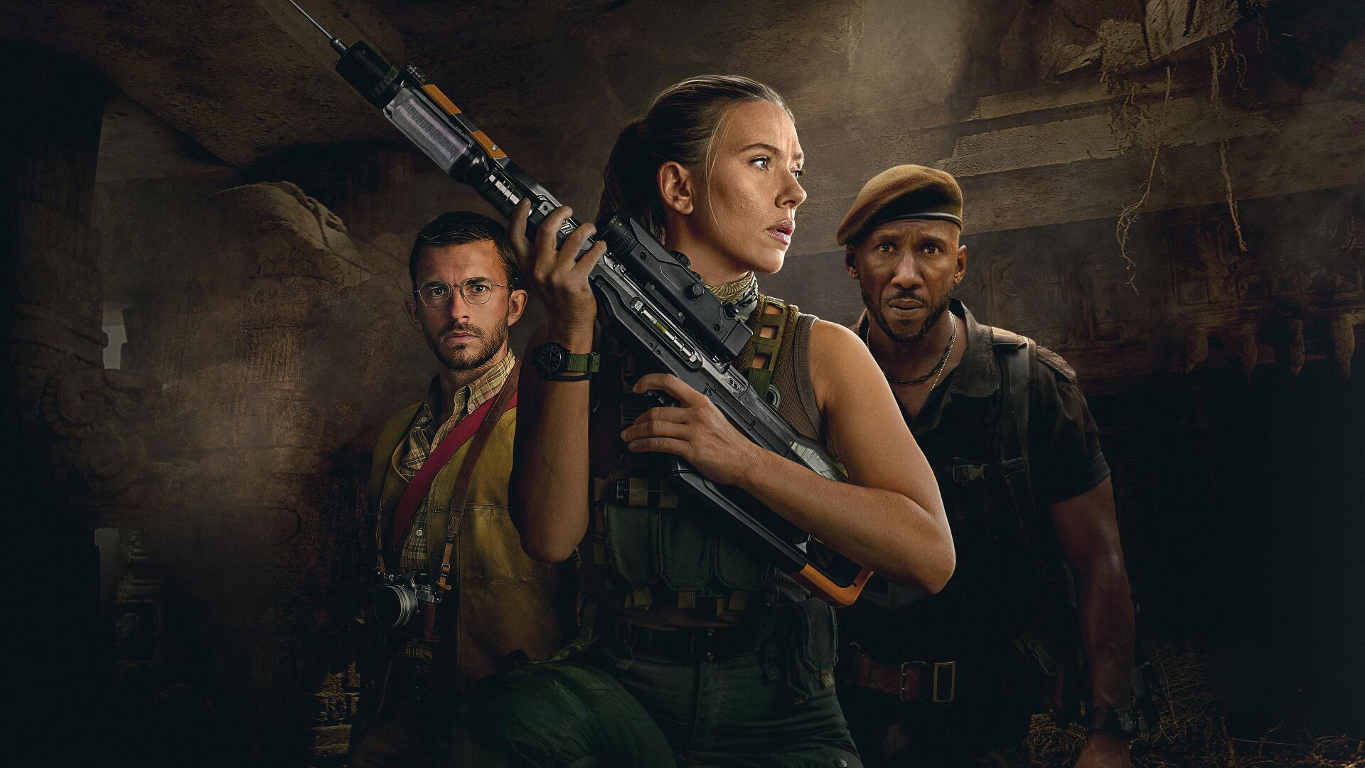 Jurassic World Rebirth 4K Ultra HD PC wallpaper: three armed survivors—central woman with rifle and two men—stand in a dim, ruined industrial room with dramatic lighting.
