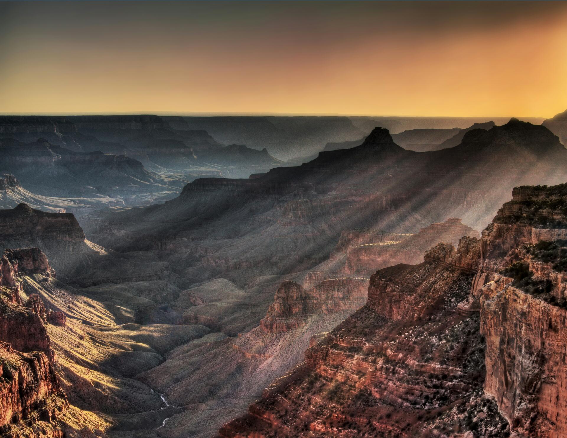 5K Ultra HD desktop wallpaper of the Grand Canyon in Arizona, USA — sun rays streaming over layered canyon ridges at sunrise.