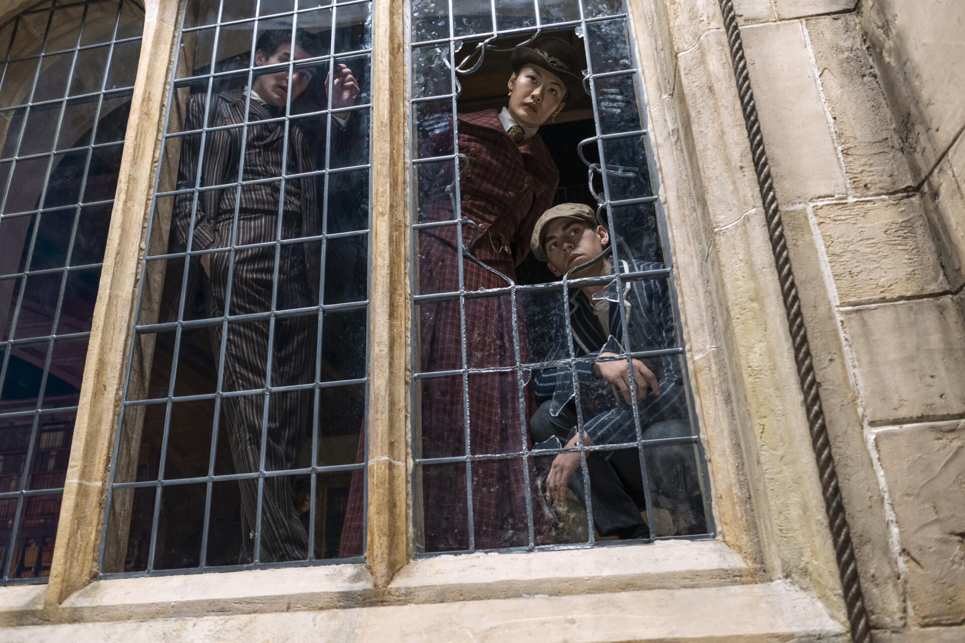 Young Sherlock (TV show) scene: two young sleuths peer from a tall leaded window framed by stone mullions — 2K Quad HD PC desktop wallpaper/background.