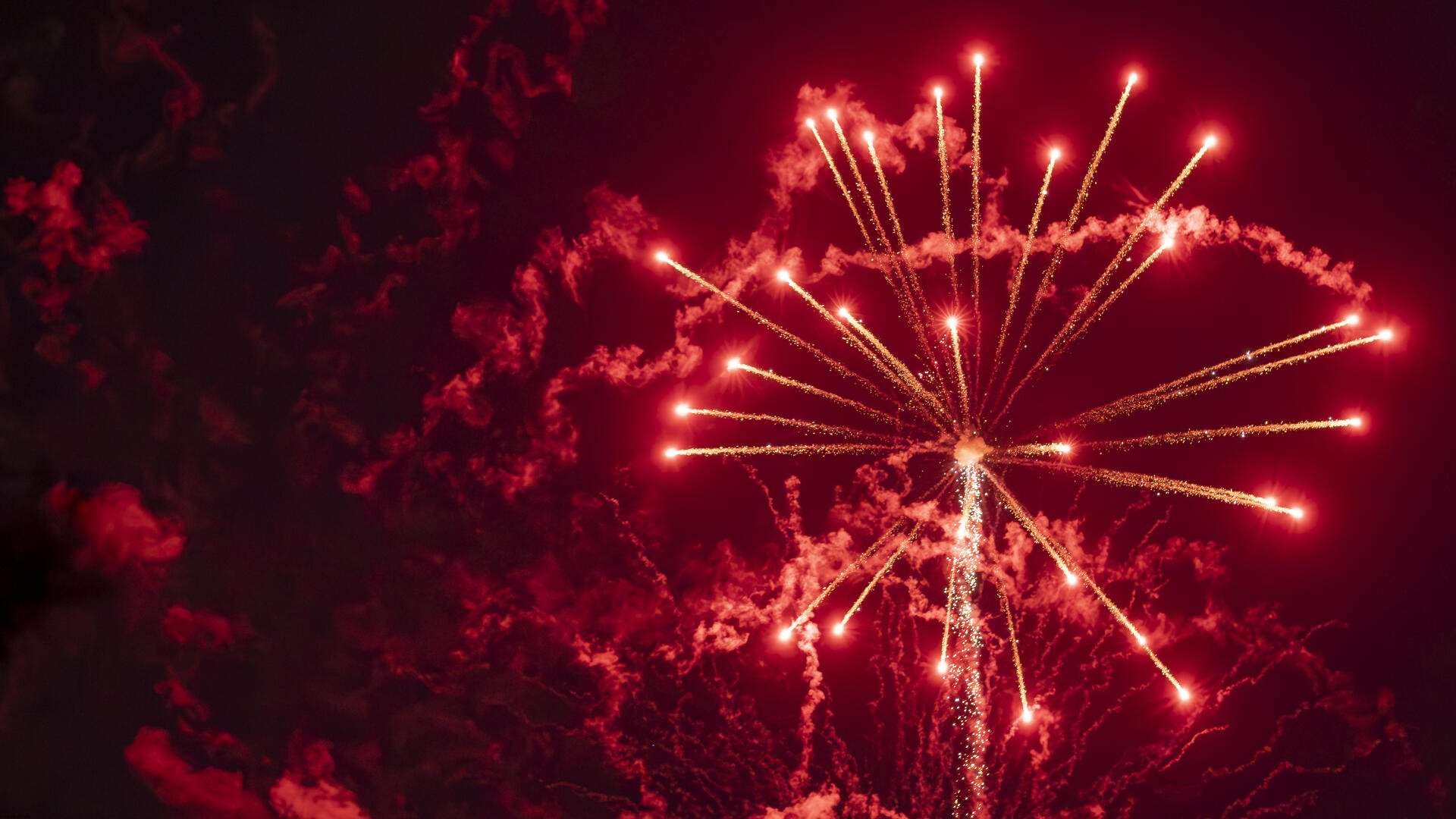 Red fireworks burst across a smoky night sky in a celebratory display — 4K Ultra HD PC desktop wallpaper and background.