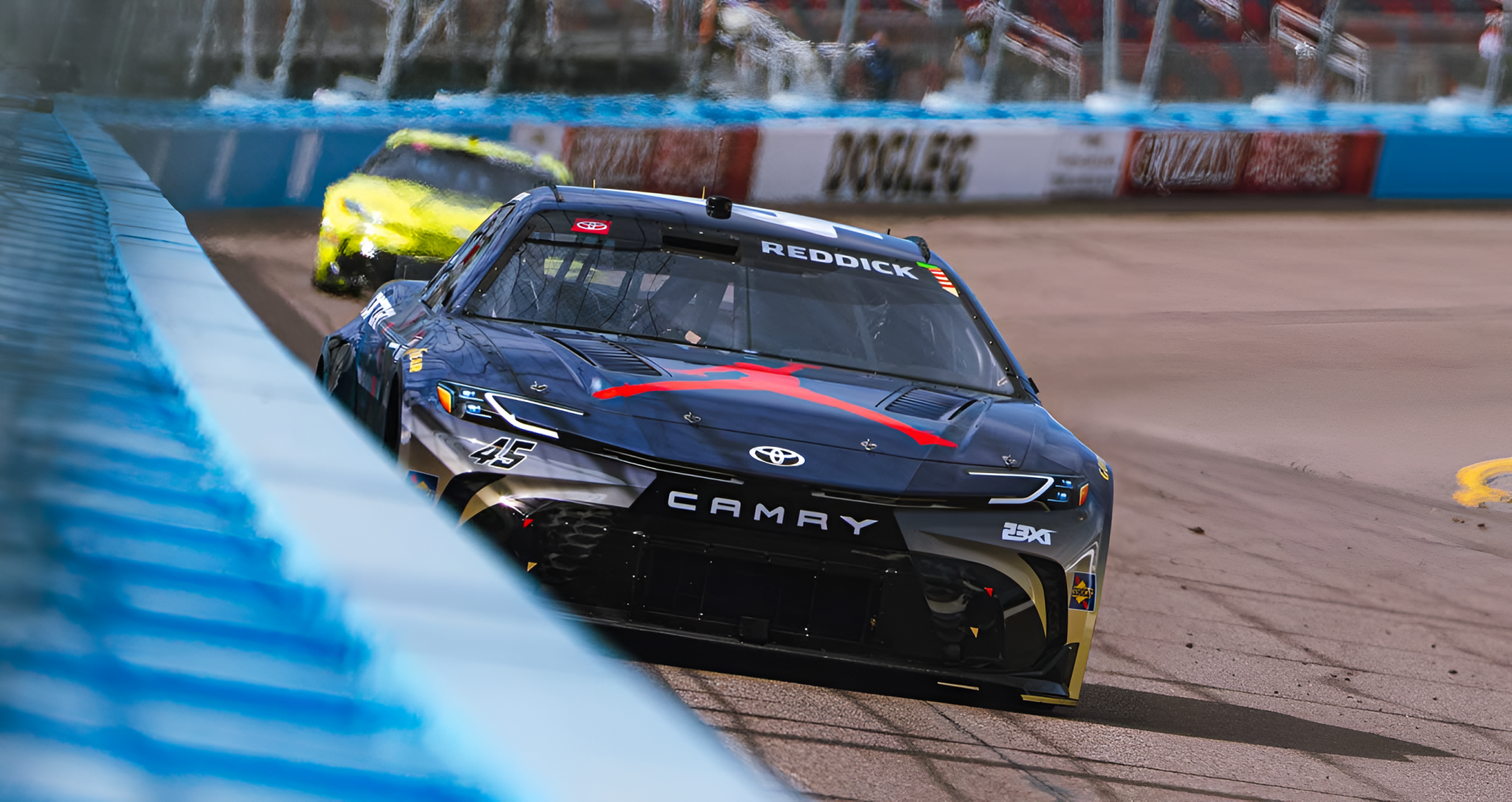HD sports PC desktop wallpaper showing a black Toyota Camry NASCAR race car speeding on the track in a close-up action shot.