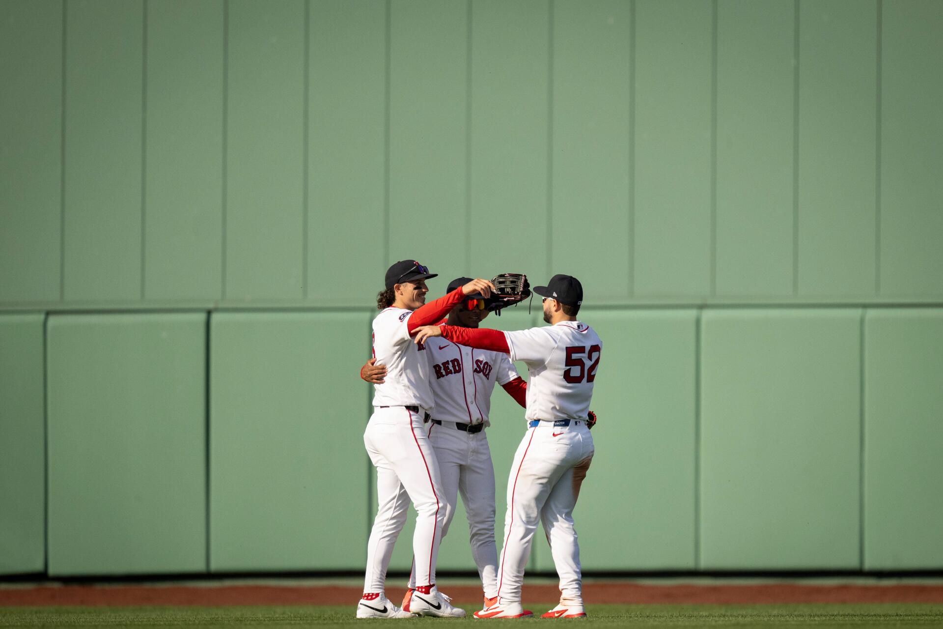 Four Boston Red Sox players embrace on the outfield grass against a green wall — 4K Ultra HD PC desktop wallpaper background, MLB baseball sports image.