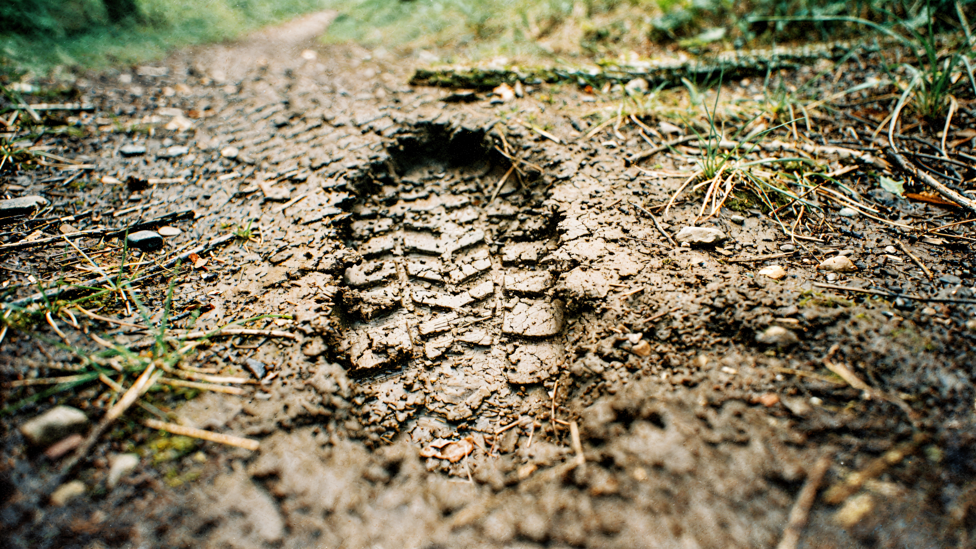Close-up of a boot print pressed into a muddy trail with grass and detailed treads — 4K Ultra HD PC desktop wallpaper and background.