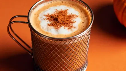 4K Ultra HD PC desktop wallpaper of a close-up pumpkin spice latte in a textured glass mug, frothy top dusted with cinnamon on a warm orange background.
