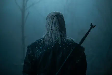 Rear view of Geralt of Rivia from The Witcher TV show, sword on his back in a misty blue forest — 8K Ultra HD PC desktop wallpaper/background.