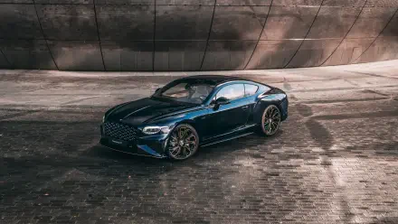 Sleek dark blue Bentley Continental GT luxury car on wet cobblestone in front of a curved concrete wall — 8K Ultra HD PC desktop wallpaper