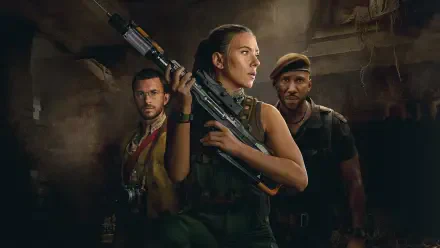 Jurassic World Rebirth 4K Ultra HD PC wallpaper: three armed survivors—central woman with rifle and two men—stand in a dim, ruined industrial room with dramatic lighting.