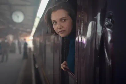 Young woman peering from a train window onto a dim underground platform — 4K Ultra HD PC wallpaper featuring an actress from Agatha Christie's Seven Dials.