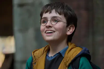 Smiling young Harry Potter from the 2027 TV show, round glasses and layered jacket, captured as an HD PC desktop wallpaper/background.