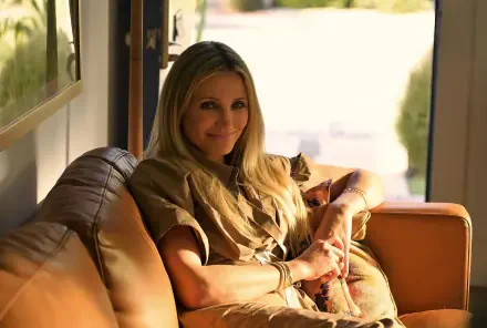 Sunlit 2K Quad HD PC desktop wallpaper: smiling actress from the movie Outcome (2026) reclining on a leather sofa in a relaxed, warm domestic scene.