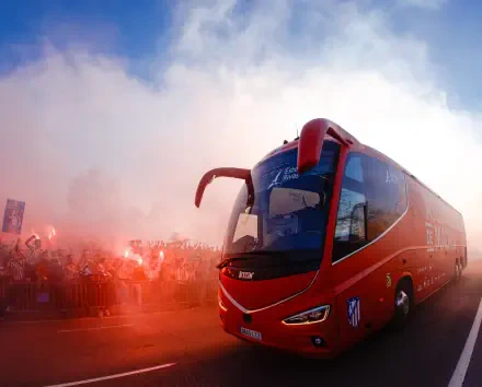 HD desktop wallpaper showing Atlético Madrid red team bus passing a cheering crowd amid red smoke and flares.