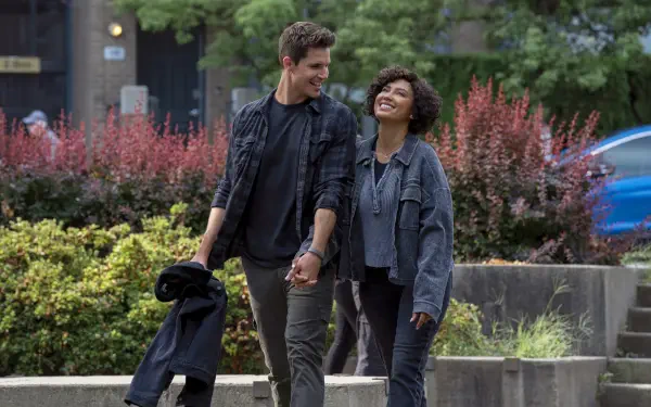 HD PC desktop wallpaper from the TV show Upload: two actors — a man and a woman — walk hand in hand through a city park, smiling and chatting.