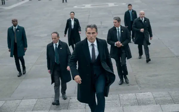 2K Quad HD PC desktop wallpaper of a suited lead from the TV show The Diplomat striding up stone steps, flanked by men in suits and security detail.