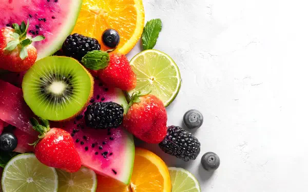 Vibrant 4K Ultra HD PC desktop wallpaper and background of mixed fruit food: sliced kiwi, lime, orange, watermelon, strawberries, blackberries and blueberries on white.