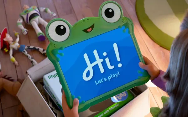 Toy Story 5 5K Ultra HD PC Desktop Wallpaper: a child holds a frog-shaped tablet that says Hi! Let's play! with Woody, Buzz and other toys in a box on a wooden floor.