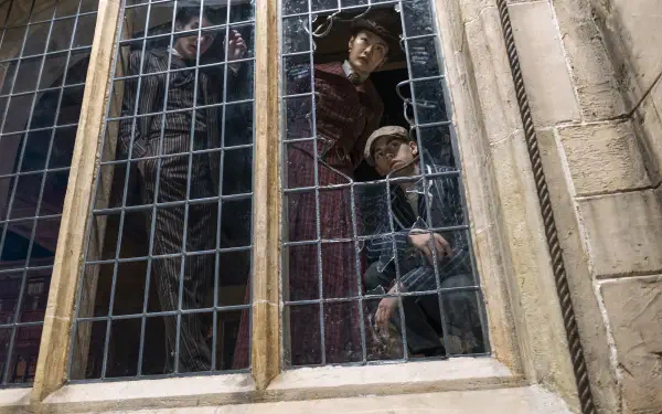 Young Sherlock (TV show) scene: two young sleuths peer from a tall leaded window framed by stone mullions — 2K Quad HD PC desktop wallpaper/background.