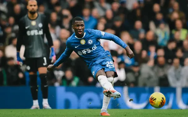 HD desktop wallpaper: Chelsea F.C. midfielder in blue kit firing a shot during a soccer match, crowd and an opponent blurred in the background.