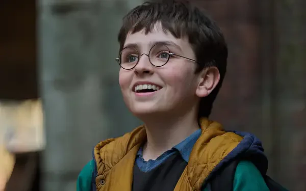 Smiling young Harry Potter from the 2027 TV show, round glasses and layered jacket, captured as an HD PC desktop wallpaper/background.
