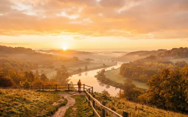 Morning sunrise over a misty river valley with autumn foliage and two figures by a fence — 5K Ultra HD PC Desktop Wallpaper and Background.