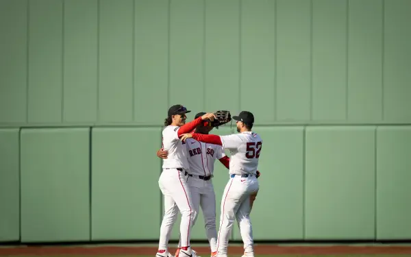 Four Boston Red Sox players embrace on the outfield grass against a green wall — 4K Ultra HD PC desktop wallpaper background, MLB baseball sports image.