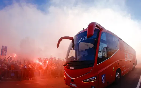 HD desktop wallpaper showing Atlético Madrid red team bus passing a cheering crowd amid red smoke and flares.